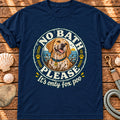 A navy blue short-sleeve t-shirt with a circular graphic of a golden retriever dog and the text 'NO BATH PLEASE It's only fox poo', displayed flat on a rustic wooden background with seashells and a leash.