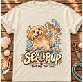 Ivory Seal Pup T-shirt laid flat on wood, featuring a golden dog with seal flippers and blue splashes and the wording “Seal Pup — Part Dog. Part Seal.”