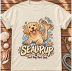 Ivory Seal Pup T-shirt laid flat on wood, featuring a golden dog with seal flippers and blue splashes and the wording “Seal Pup — Part Dog. Part Seal.”