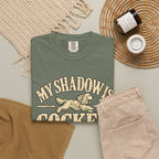 Moss T-shirt with the Cocker Spaniel illustration and “My shadow is cocker shaped” lettering, styled with beige trousers and coffee.