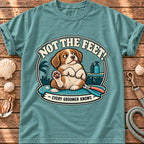 Front view of a Brinehound T-shirt showing a dog on a grooming table beneath Not the Feet lettering.
