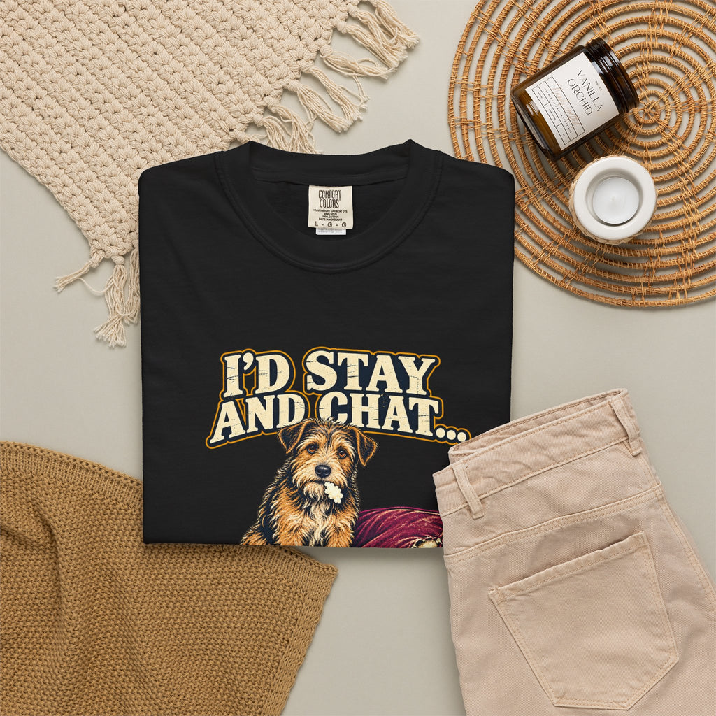 Black T-shirt with the scruffy terrier beside a chewed sofa and “I’d stay and chat” lettering print, styled with beige trousers and coffee.