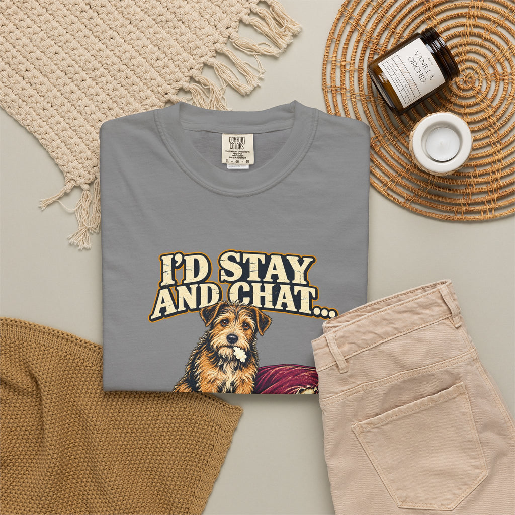 Grey T-shirt with the scruffy terrier beside a chewed sofa and “I’d stay and chat” lettering print, styled with beige trousers and coffee.