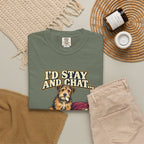 Moss T-shirt with the scruffy terrier beside a chewed sofa and “I’d stay and chat” lettering print, styled with beige trousers and coffee.