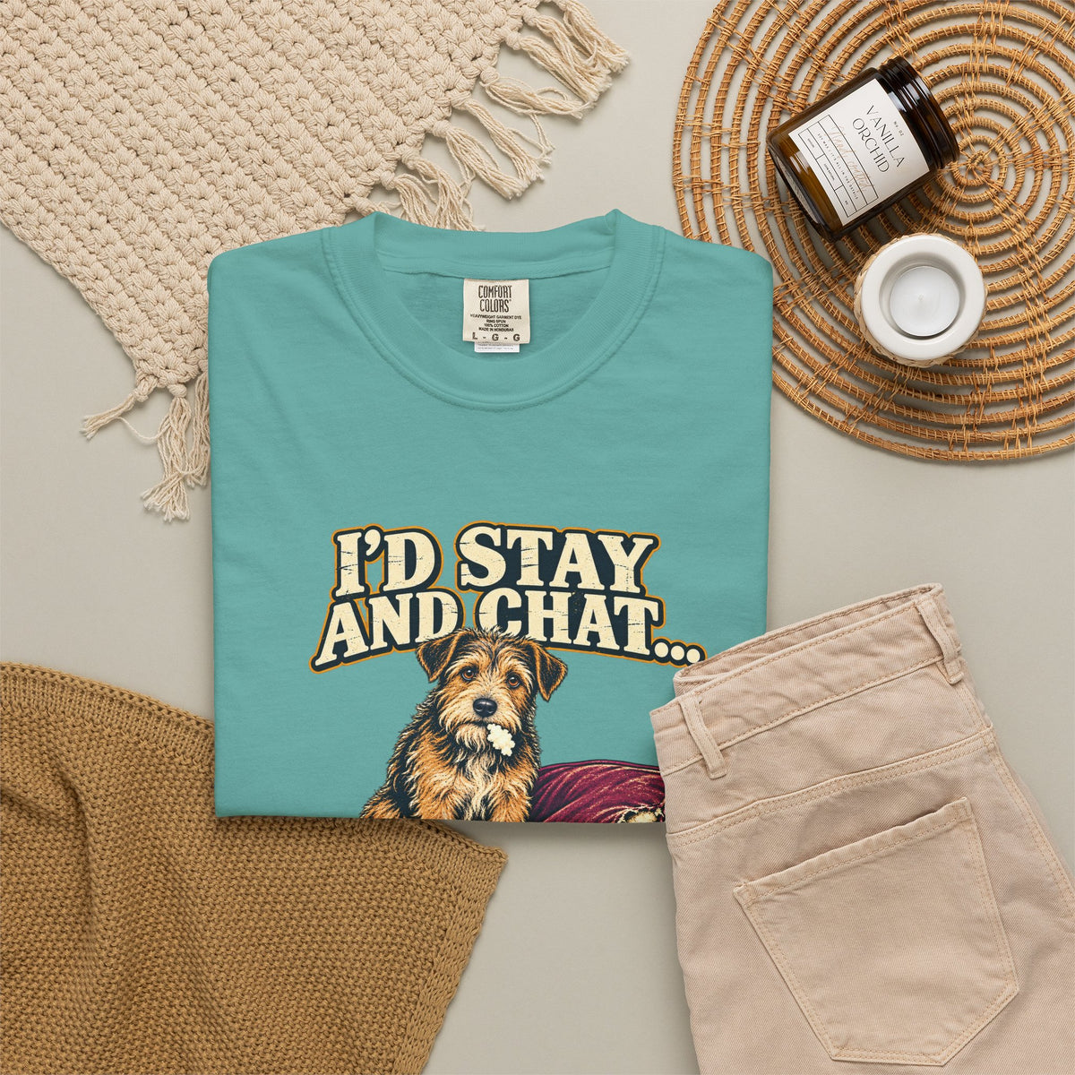 Seafoam T-shirt with the scruffy terrier beside a chewed sofa and “I’d stay and chat” lettering print, styled with beige trousers and coffee.
